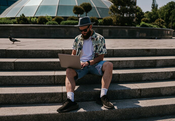Photo of a freelance web designer young guy working outdoors on a laptop computer connected to a...