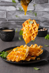 Flying waffles and mint getting dropped with mango jam a grey background