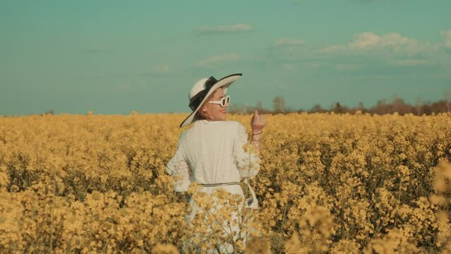 Beautiful young woman in white dress on yellow flower meadow in sunset