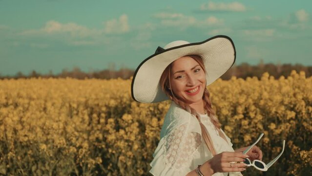 Beautiful young woman in white dress on yellow flower meadow in sunset