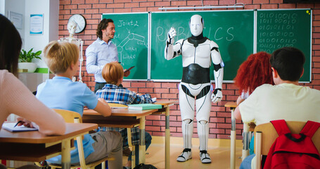 Caucasian male teacher with digital tablet in hands showing humanoid droid to curios children at school. Pupils listening attentively about software programming works of robotics