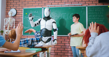 Schoolboy with futuristic white robot standing near blackboard and waving hands to classmates....