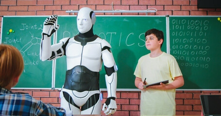 Caucasian teen schoolboy shaking hands with robot at blackboard in classroom. Technology learning....