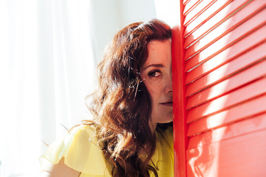 Beautiful Brunette Woman In A Yellow Dress Sits By The Window With A Red Screen