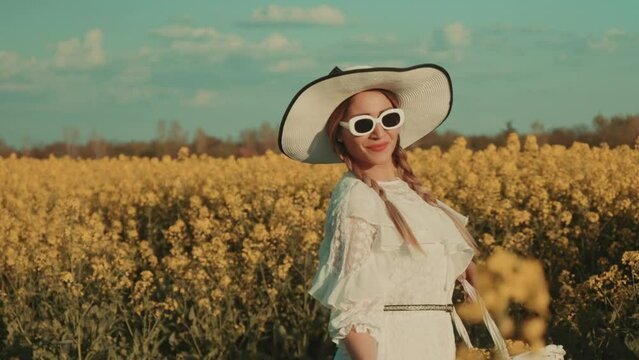 Beautiful young woman in white dress on yellow flower meadow in sunset