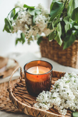 Obraz na płótnie Canvas Burning candle and basket of white lilacs in home interior