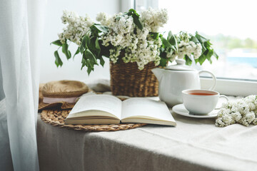 Open book, cup of tea and teapot, white lilac basket and hat, summer composition
