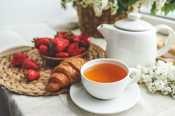 Cup of tea, croissant, strawberry and lilac basket, summer morning aesthetic