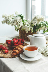 Cup of tea, croissant, strawberry and lilac basket, summer morning aesthetic