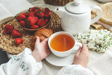 Cup of tea in hands, strawberries and flowers, summer breakfast concept
