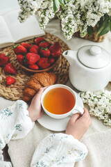 Cup of tea in hands, strawberries and flowers, summer breakfast concept