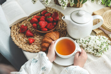 Cup of tea in hands, strawberries and flowers, summer breakfast concept