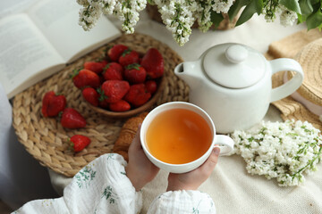 Cup of tea in hands, strawberries and flowers, summer breakfast concept