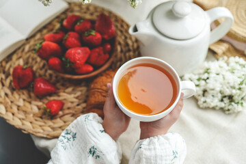 Cup of tea in hands, strawberries and flowers, summer breakfast concept