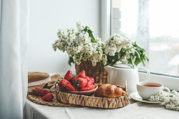 Cup of tea, croissant, strawberry and lilac basket, summer morning aesthetic