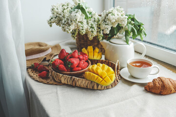 Cup of tea, croissant, strawberry and lilac basket, summer morning aesthetic