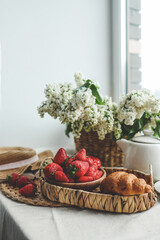 Cup of tea, croissant, strawberry and lilac basket, summer morning aesthetic