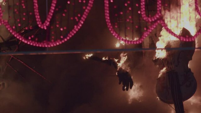 The tradition of Fallas on the streets of Valencia, Spain involves the burning of large and colorful ninot figures against the backdrop of the night sky. Burning hand visible