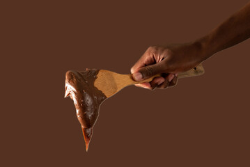 hand holding wooden spoon with brigadeiro on brown background