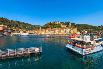 Wooden pier and a fishing boat moored in the famous port of Portofino, luxury Tourist resort in Genoa Province, Liguria, Italy, Europe. Colorful houses, Mediterranean sea (Ligurian sea). - obrazy, fototapety, plakaty