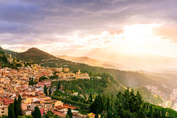 travel landscape of a highland mediterranean town with yellow buildings, green trees and gardens, beautiful mountains and amazing cloudy sunset