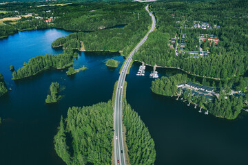 Aerial view of asphalt road with cars over blue lake and green woods in Finland