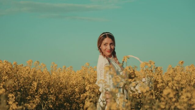 Beautiful young woman in white dress on yellow flower meadow in sunset