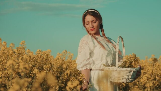 Beautiful young woman in white dress on yellow flower meadow in sunset