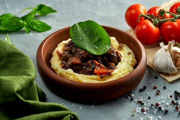 Mashed potatoes with stewed meat in a clay dish on a concrete background