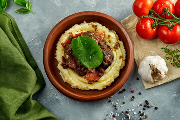 Mashed potatoes with stewed meat in a clay dish on a concrete background