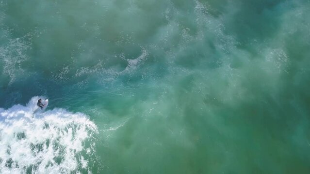Top down aerial view of surfer taking off on wave carving and spraying on wave