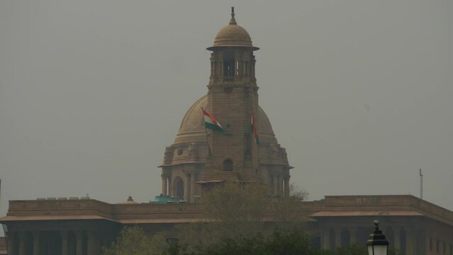 Indian flags waving at the top of the government building at Kartavya Path in poor air quality, low visibility, grey smog sky, New Delhi, India