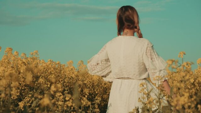 Beautiful young woman in white dress on yellow flower meadow in sunset