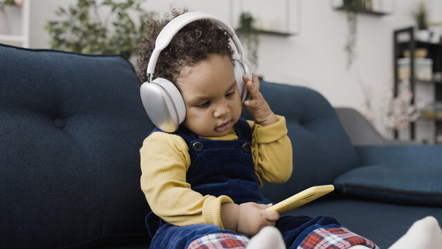 Sweet little baby pretends to listen to music while holding a smartphone and wearing large headphones