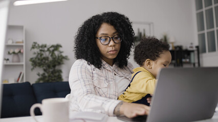 Tired African American woman working and babysitting her son, unpaid maternity leave