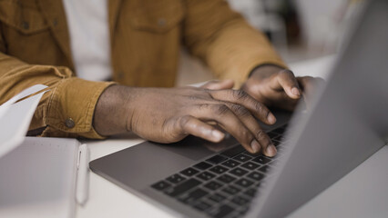 Close-up of African American man typing on laptop keypad, working on a project
