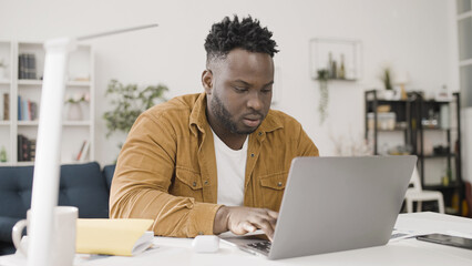 Concentrated African American man working on laptop at home office, freelance