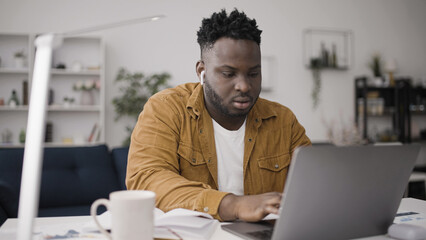 African American man working on project on laptop, sitting in cozy home office