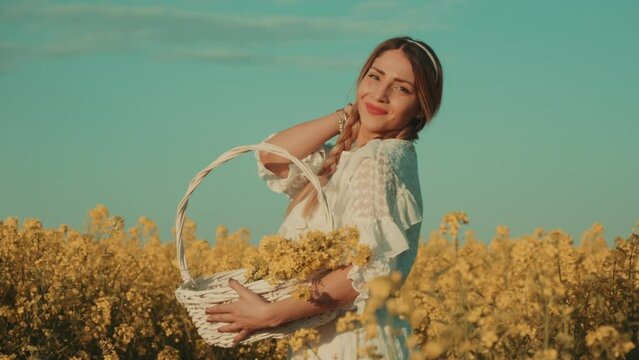 Beautiful young woman in white dress on yellow flower meadow in sunset