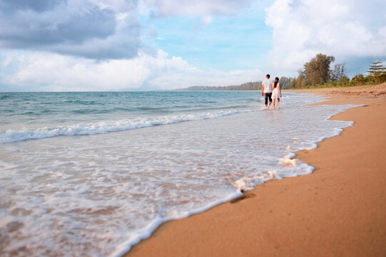 Honeymoon at the sea. Back view of loving couple walking away at sandy beach