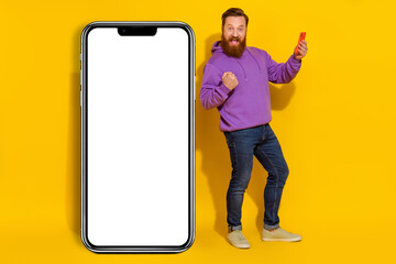 Full size photo of delighted positive person raise fist triumph empty space large phone isolated on yellow color background