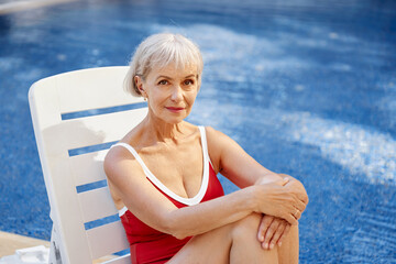 Happy vacation. Senior woman in red swimwear on the sunlounger near the swimming pool.