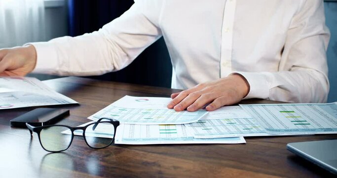 The trader sorts through important papers with numbers and data, financial monitoring on paper.