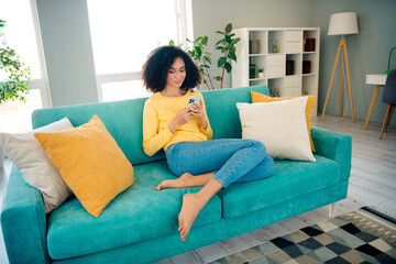 Photo of cheerful woman with perming coiffure wear yellow long sleeve sitting on couch choose new furniture online at home room indoors