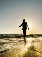 Low angle view of woman walking in backlit on a beach at sunset.