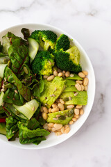 Healthy breakfasts, chard salad with beans and cucumbers, avocado and broccoli sprinkled with different seeds, a plate with food on a white marble background