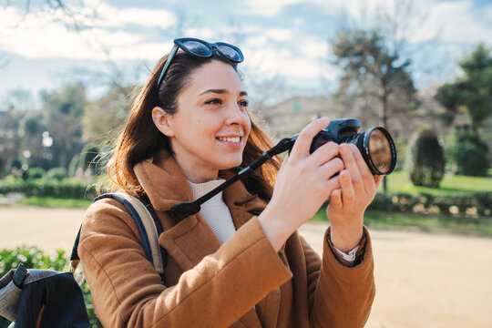 young female photographer smiling and shooting a artistic photo on a weekend travel activity. One caucasian hipster woman enjoying taking a pic with a retro professional camera on a vacation trip