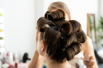 Fototapeta premium The hairdresser curls the model's hair. Curling iron for curling hair close-up.