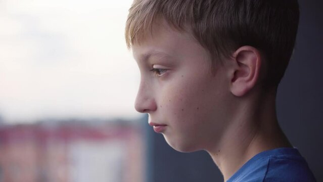A cute young boy looks out a balcony and thinks about something - face closeup from the side