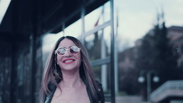 Beautiful attractive young happy woman walking with confidence outdoor infront of office building smiling and playing with the camera looking stylish and sexy
